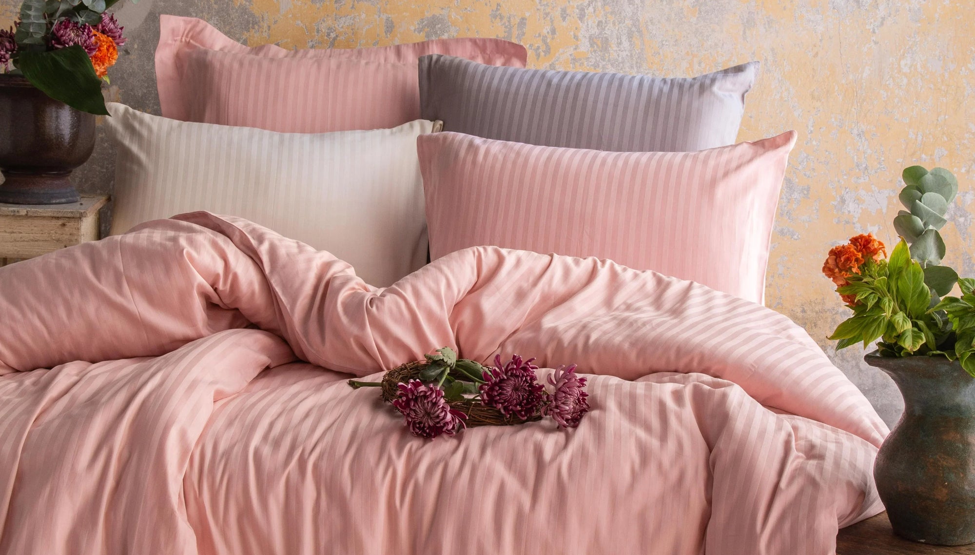 Striped pink and cream bedding set with pillows and fresh flowers on a rustic bed