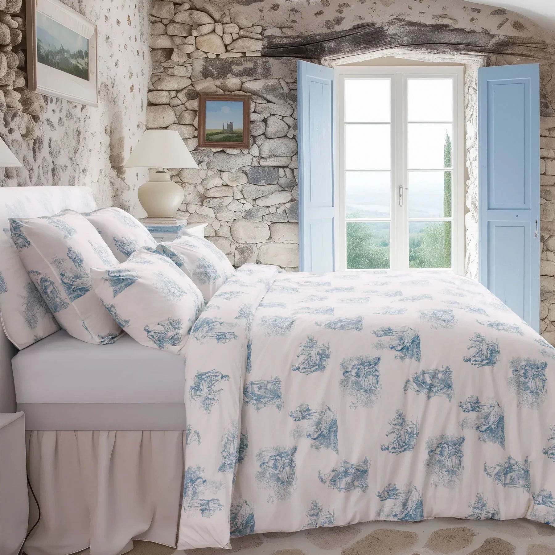 Blue and white toile de Jouy duvet cover set in rustic stone-walled bedroom with window